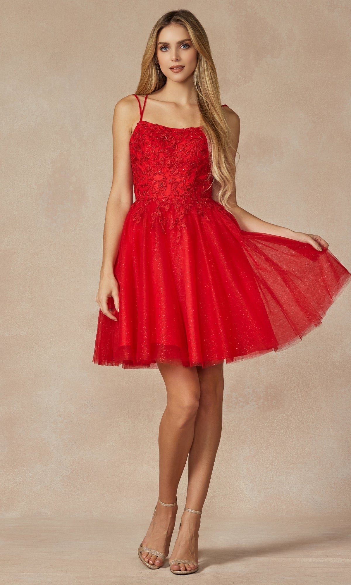 A woman wears the Embroidered-Corset Babydoll Homecoming Dress 860—a sleeveless, short red dress with lace details and a flared tulle skirt—paired with nude heels and holding one side of the skirt.